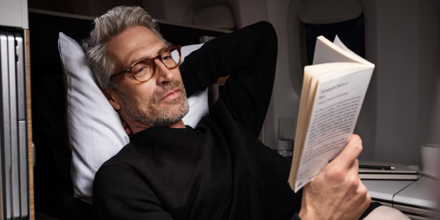 Uomo che legge un libro a bordo di un aereo.